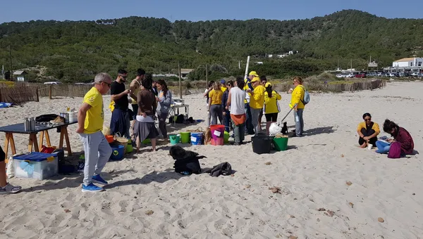 Voluntarios con chaleco amarillo de Voluntaris d'Eivissa clasificando residuos en cubos y cestas