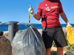 Voluntario pesando una bolsa de basura grande con una báscula de mano junto al mar