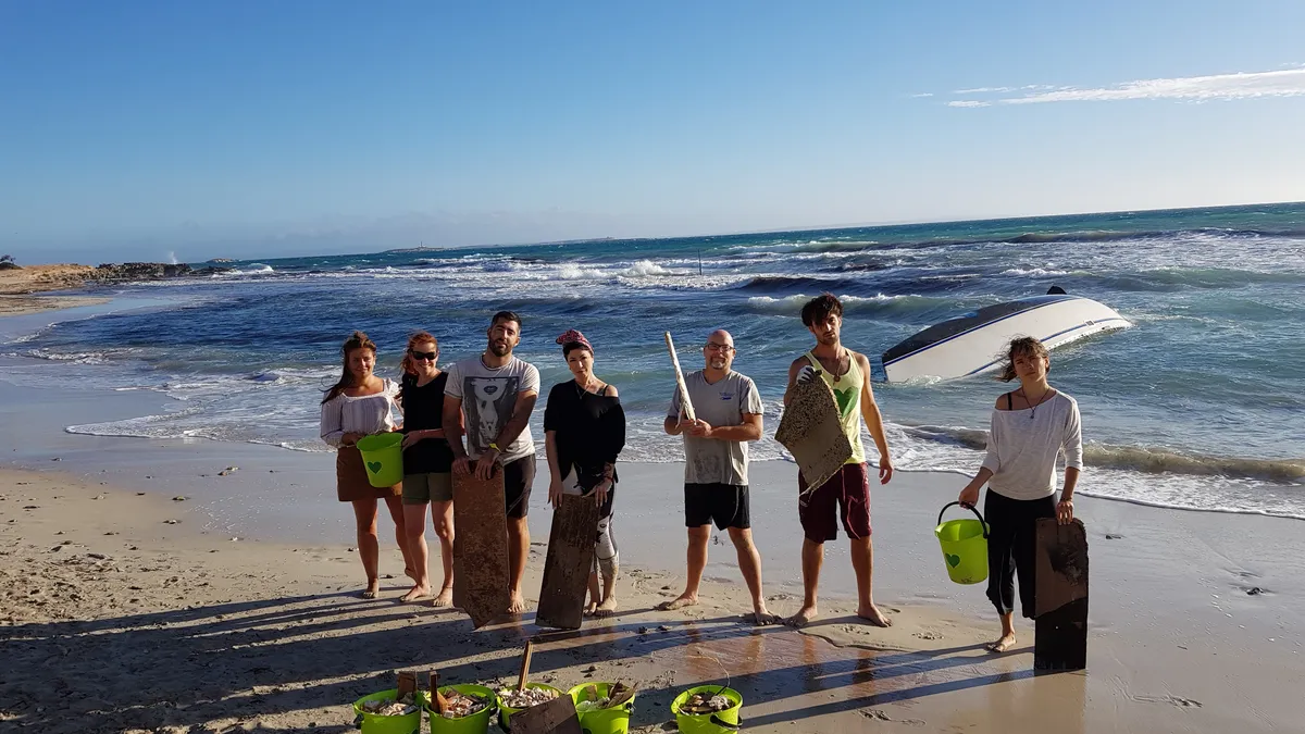 Grupo de voluntarios de One Planet One Life con cubos verdes tras una limpieza de playa en 2019