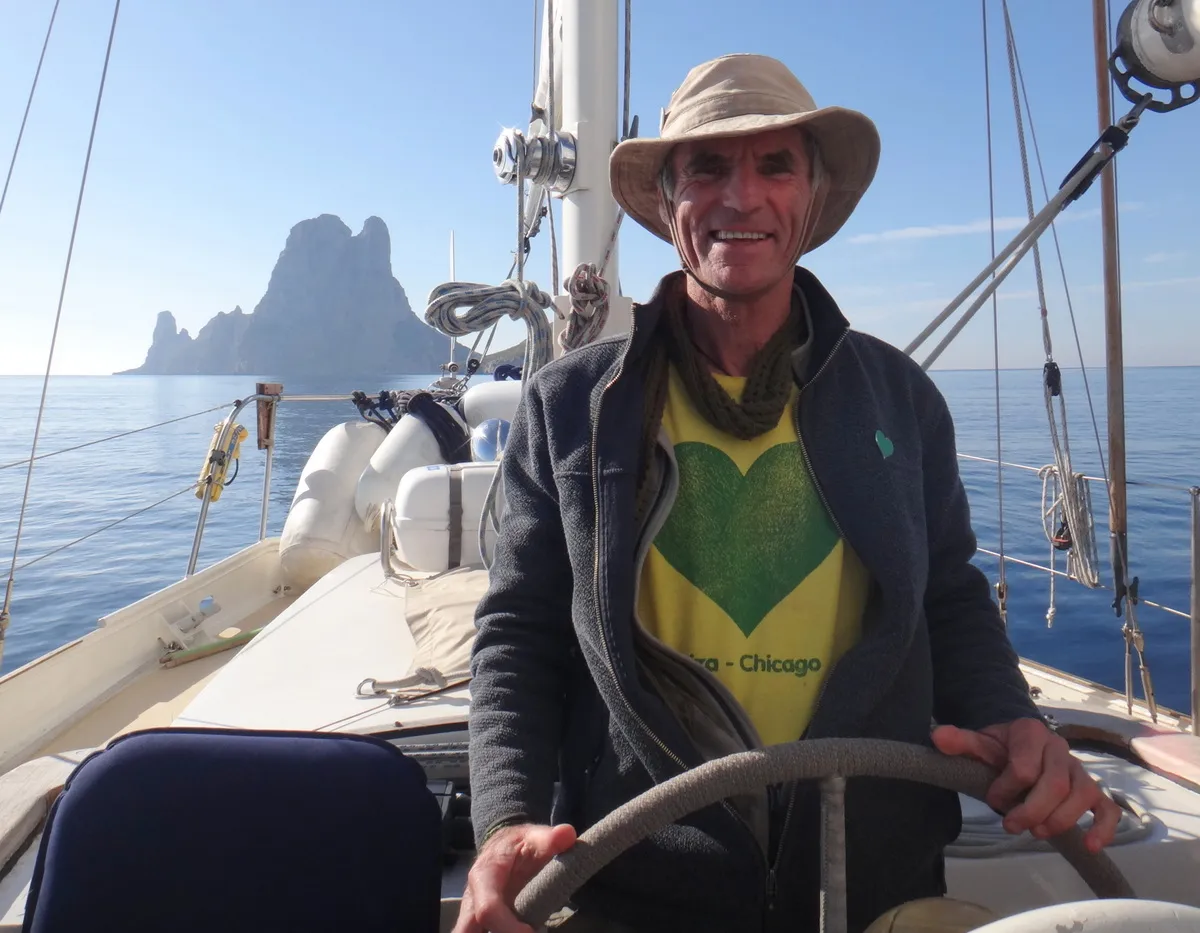 Chris Dews al timón de un velero, con Es Vedrà al fondo