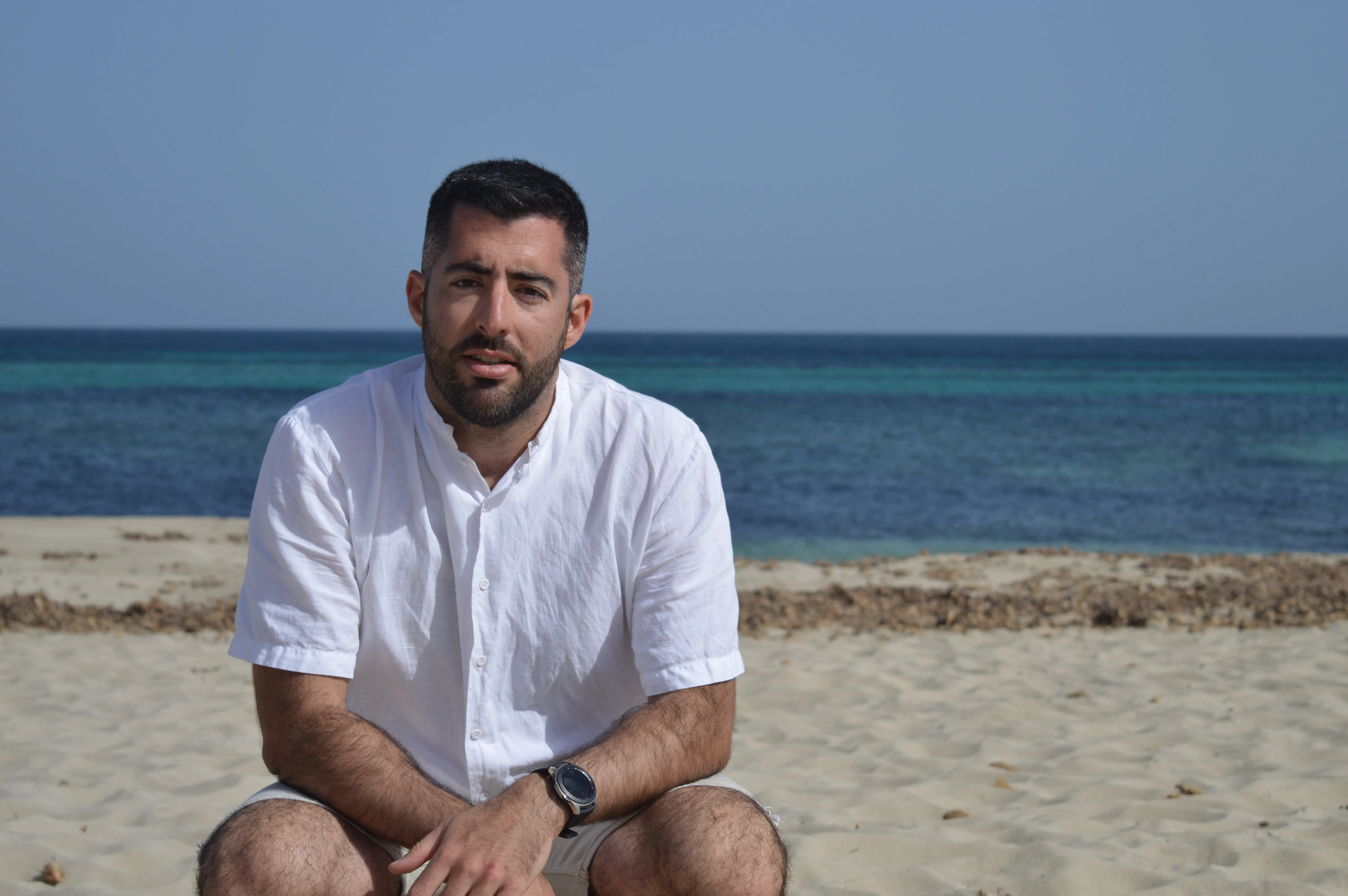 Diego de la Viña sentado en la arena, con el mar de fondo